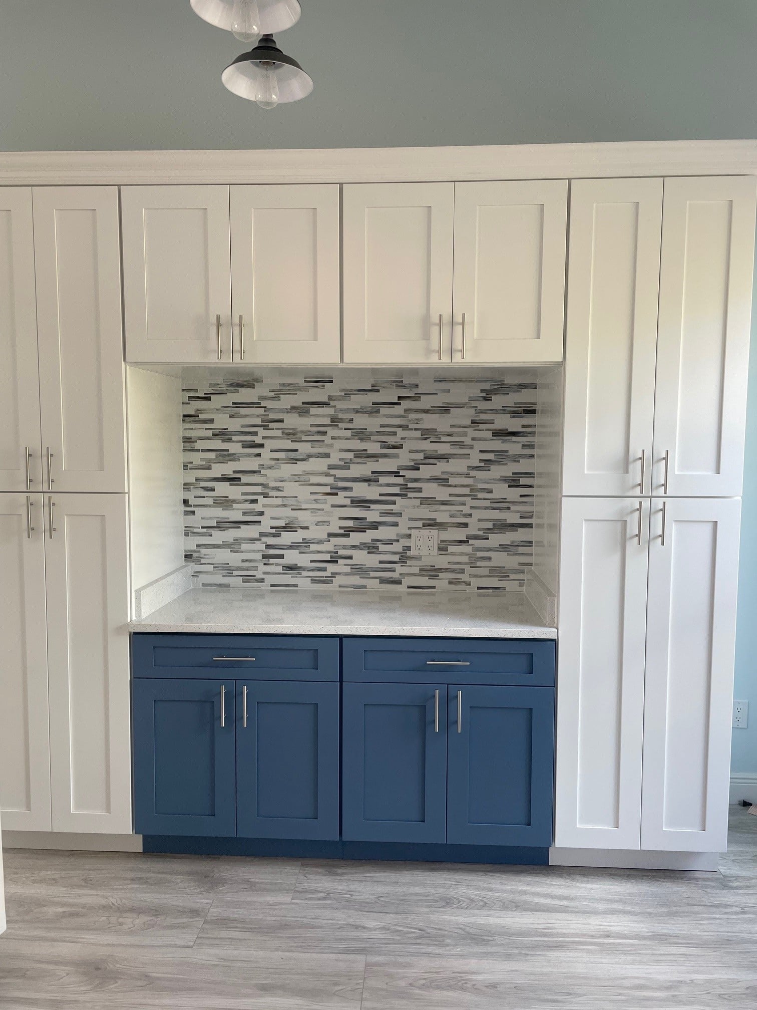 An installed bar: upper cabinets either side, tiled backsplash, stone counter and base cabinets below